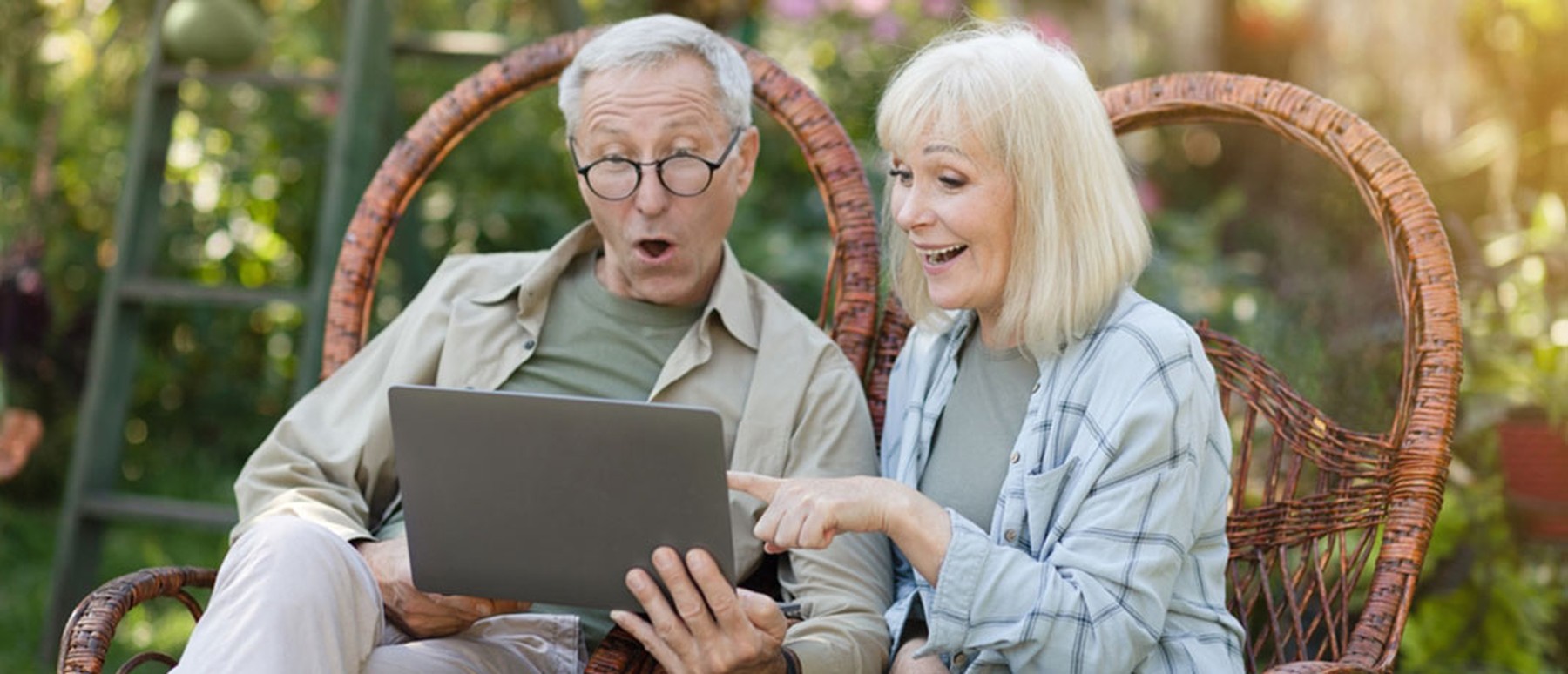 Older Couple Sitting in Chairs Outside Looking at Computer