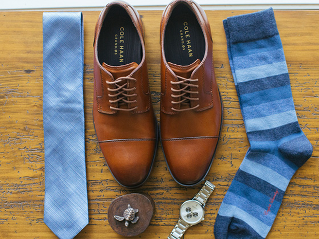 Cole Haan shoes sitting by a blue tie, blue striped socks, and a watch